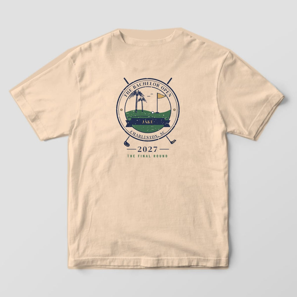 Back of an Ivory Comfort Colors tee with a round golf seal, crossed clubs, palmettos, gold flag, the name JAKE, 2027 and THE FINAL ROUND