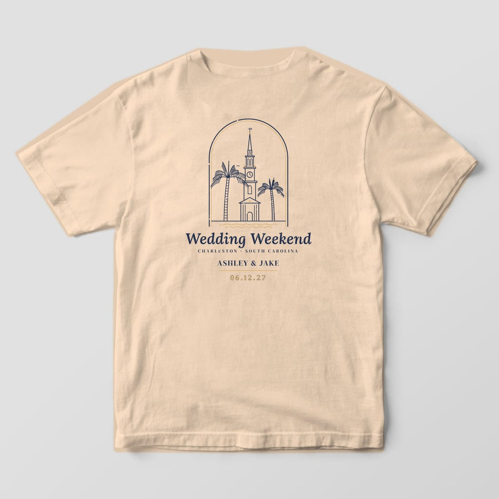 Back of an Ivory Comfort Colors tee with a line-art steeple and two palmettos in an arched frame above Wedding Weekend, Charleston SC, names and date